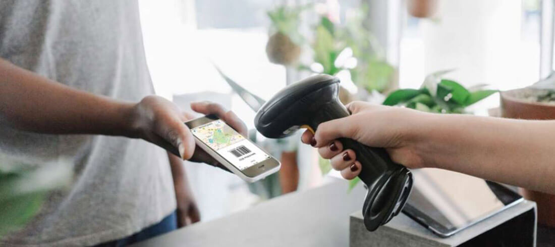 Eine Hand hält ein Smartphone mit Code zum Bargeldabheben vor einen Scanner einer Supermarktkasse.