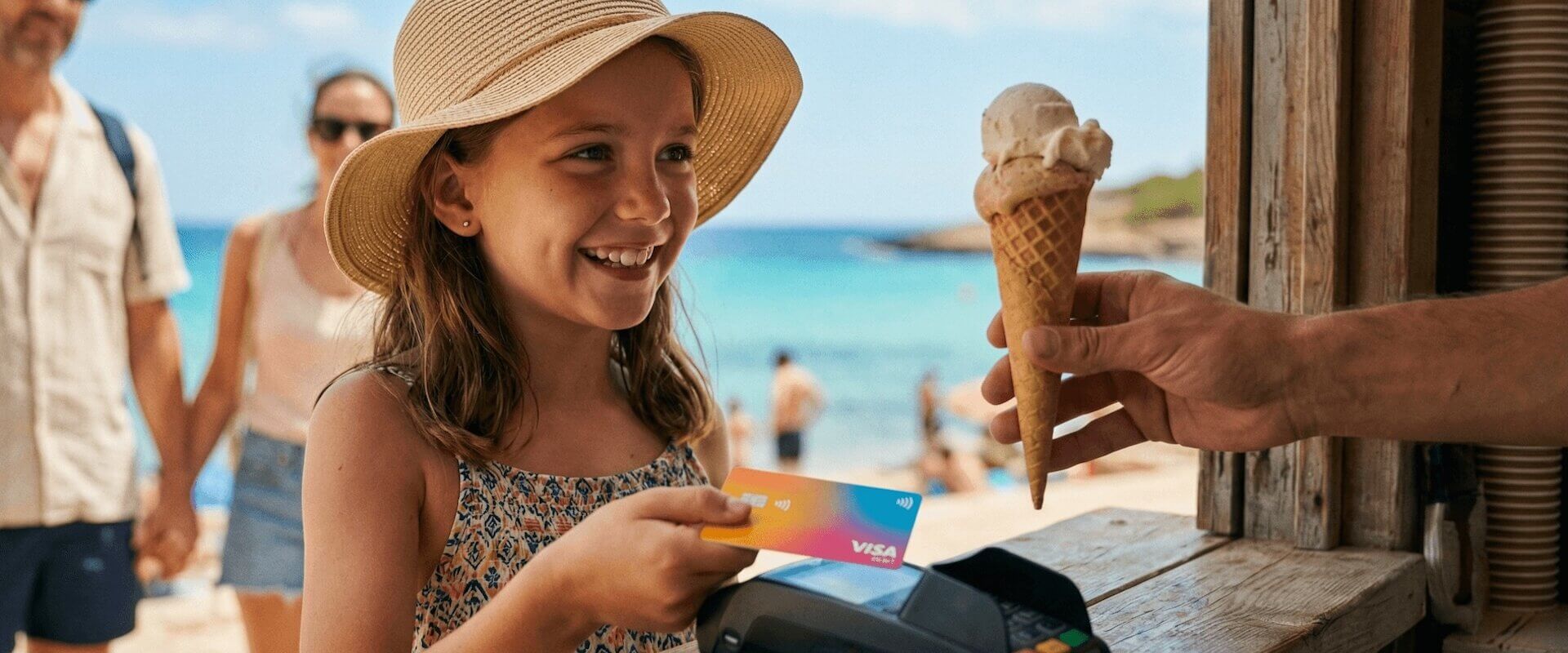 Mädchen (ca. 10) kauft sich am Strandkiosk in Spanien ein Eis und hält ihre bunte Visa-Debitkarte ans Kontaktlos-Terminal. Eltern unscharf im Hintergrund, türkisblaues Meer, Sonnenhut, Sommerkleid. Strahlendes Lächeln – der stolze Moment, zum ersten Mal selbst im Urlaub zu bezahlen.