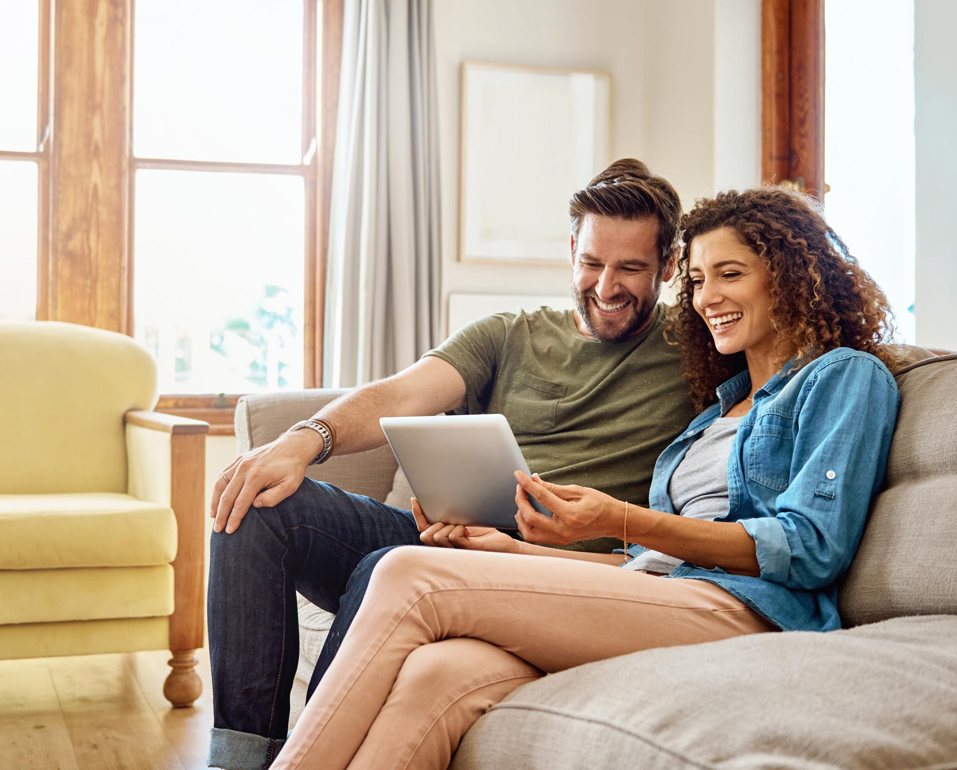 Junges Paar sitzt auf dem Sofa und plant die Geldanlage für ihr Kind auf einem Tablet