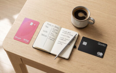 Pinke Finom Visa Business Karte und schwarze Qonto Mastercard auf einem Holztisch neben handschriftlichem Vergleichs-Notizbuch und Kaffeetasse