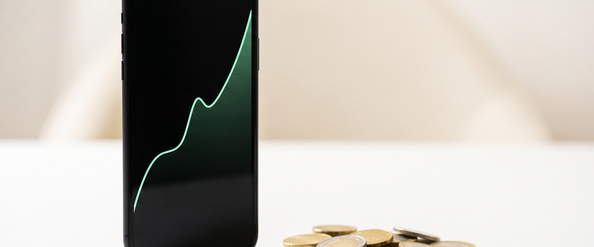 Smartphone mit steigendem Aktienchart neben Euro-Münzen, Symbol für die neue N26-Ordergebühr