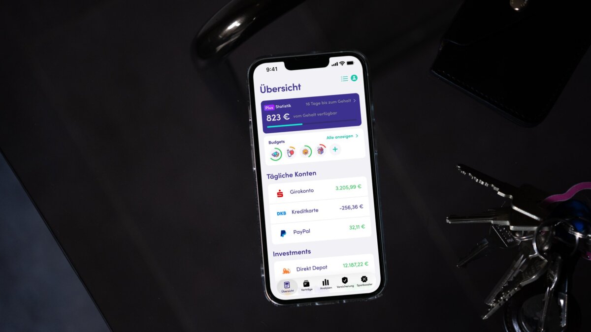 Finanzguru-App auf einem Smartphone neben Schlüsselbund und Geldbörse (Bild: Finanzguru)