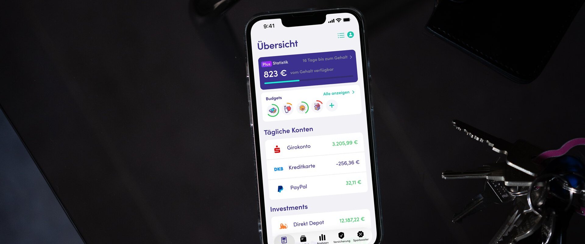 Finanzguru-App auf einem Smartphone neben Schlüsselbund und Geldbörse (Bild: Finanzguru)